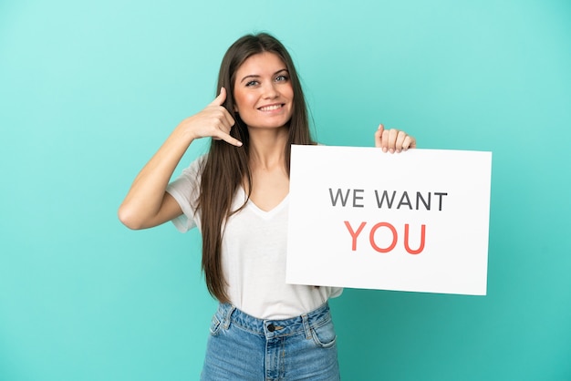 Foto giovane donna caucasica isolata su priorità bassa blu che tiene la scheda di we want you e che fa gesto del telefono