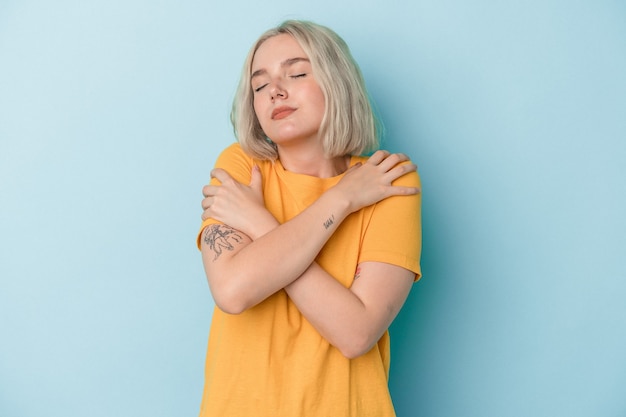 Young caucasian woman isolated on blue background hugs, smiling carefree and happy.
