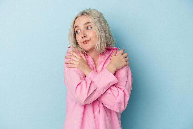 Young caucasian woman isolated on blue background hugs, smiling carefree and happy.