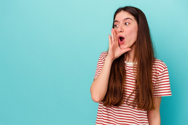 Young caucasian woman isolated on blue background is saying a secret hot braking news and looking aside