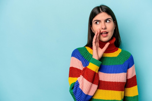 Young caucasian woman isolated on blue background is saying a secret hot braking news and looking aside