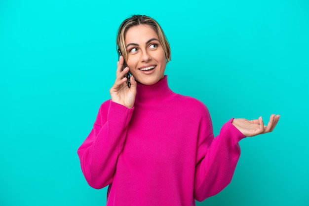 Young caucasian woman isolated on blue background keeping a conversation with the mobile phone with someone