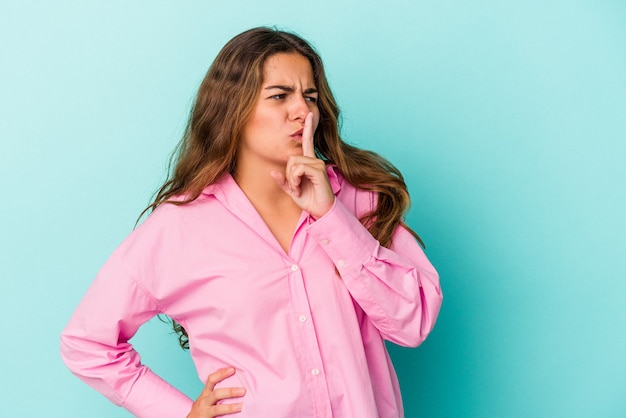 Young caucasian woman isolated on blue background  keeping a secret or asking for silence.