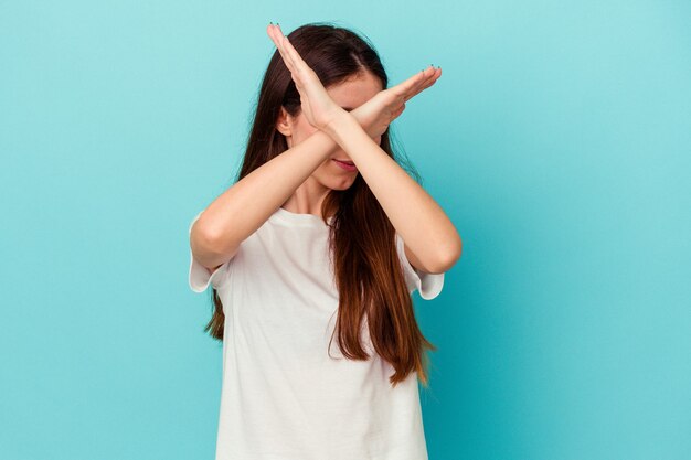 Young caucasian woman isolated on blue background keeping two arms crossed, denial concept.