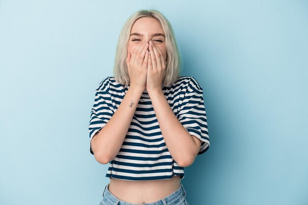 Young caucasian woman isolated on blue background laughing about something, covering mouth with hands.