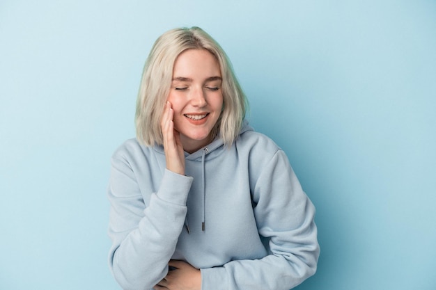 Photo young caucasian woman isolated on blue background laughs happily and has fun keeping hands on stomach