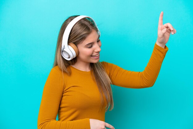 Young caucasian woman isolated on blue background listening music and dancing