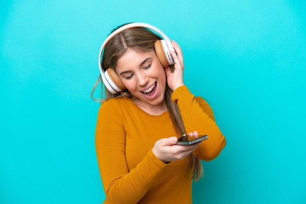 Young caucasian woman isolated on blue background listening music with a mobile and singing