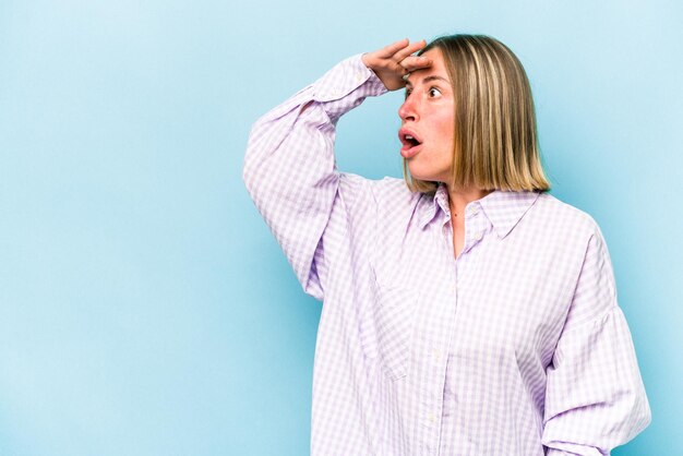 Young caucasian woman isolated on blue background looking far away keeping hand on forehead