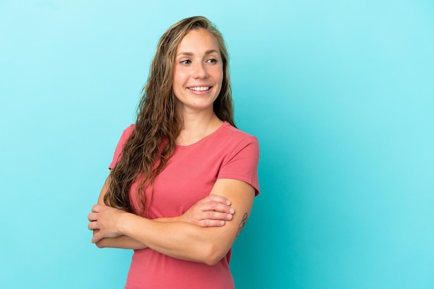 Young caucasian woman isolated on blue background looking to the side and smiling