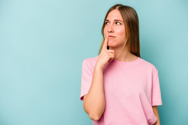 young caucasian woman isolated on blue background looking sideways with doubtful and skeptical expression