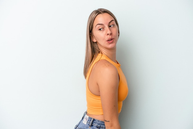 Young caucasian woman isolated on blue background looks aside smiling, cheerful and pleasant.