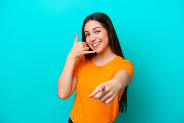 Foto giovane donna caucasica isolata su sfondo blu che fa il gesto del telefono e indica la parte anteriore