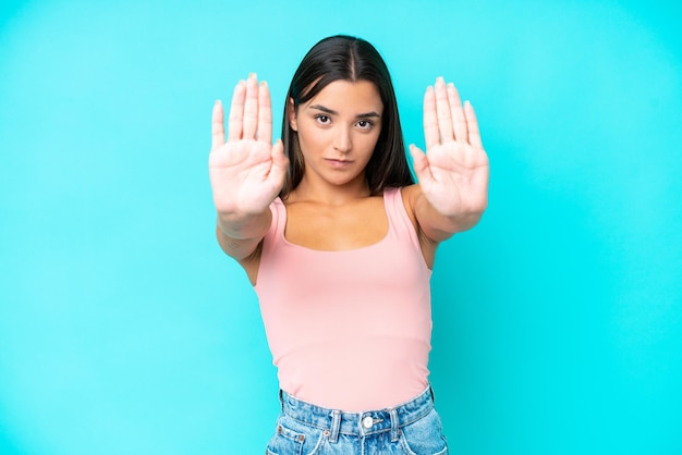 Young caucasian woman isolated on blue background making stop gesture and disappointed