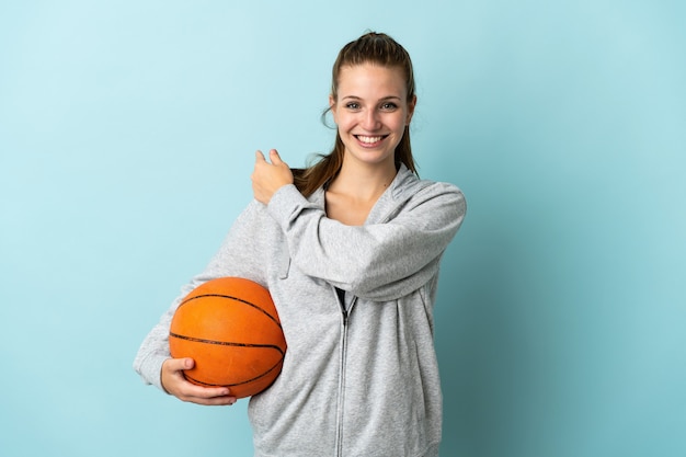 Young caucasian woman isolated on blue background playing basketball and pointing to the lateral