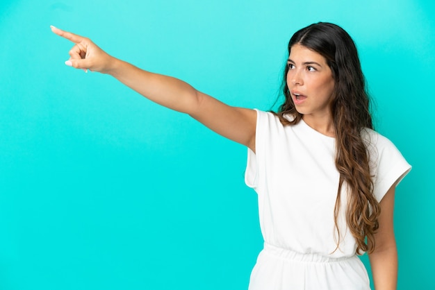 Young caucasian woman isolated on blue background pointing away