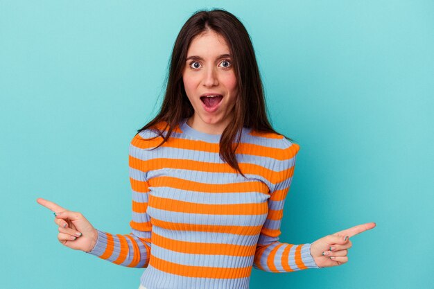 Young caucasian woman isolated on blue background pointing to different copy spaces, choosing one of them, showing with finger.