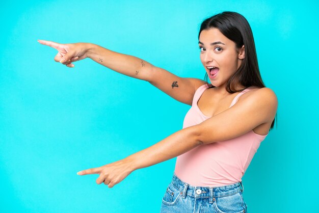 Young caucasian woman isolated on blue background pointing finger to the side and presenting a product