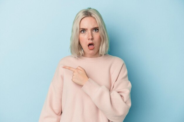 Young caucasian woman isolated on blue background pointing to the side