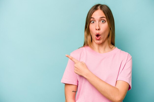 Young caucasian woman isolated on blue background pointing to the side