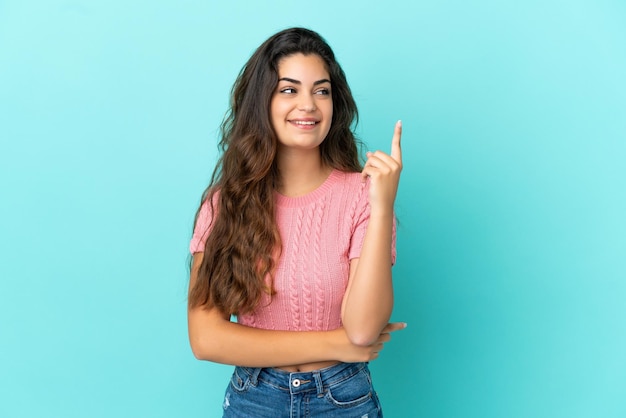 Young caucasian woman isolated on blue background pointing up a great idea