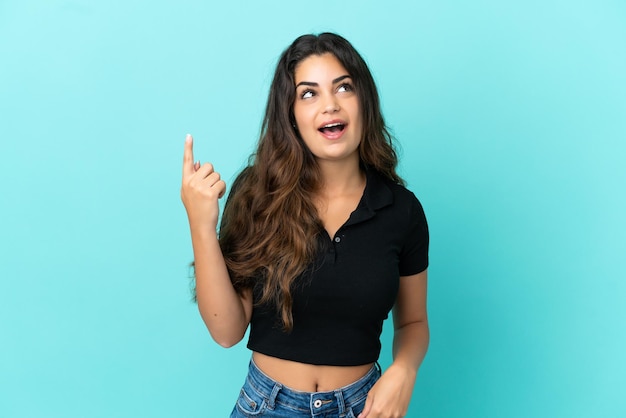 Young caucasian woman isolated on blue background pointing up and surprised