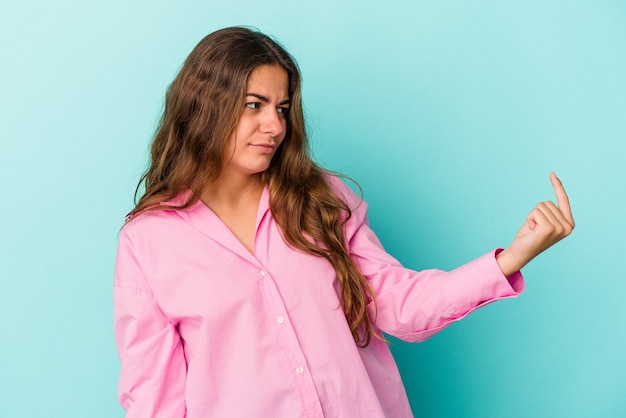 Young caucasian woman isolated on blue background  pointing with finger at you as if inviting come closer.