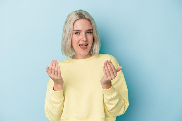 Young caucasian woman isolated on blue background pointing with finger at you as if inviting come closer.