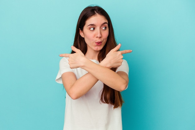 Young caucasian woman isolated on blue background points sideways, is trying to choose between two options.