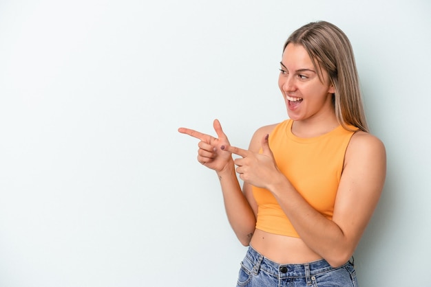 Young caucasian woman isolated on blue background points with thumb finger away, laughing and carefree.