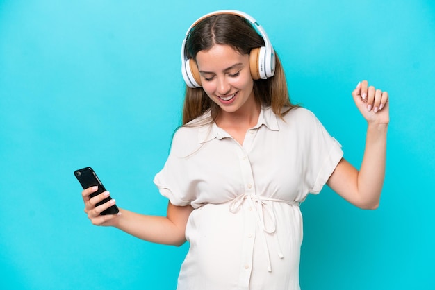 Young caucasian woman isolated on blue background pregnant and dancing while listening music
