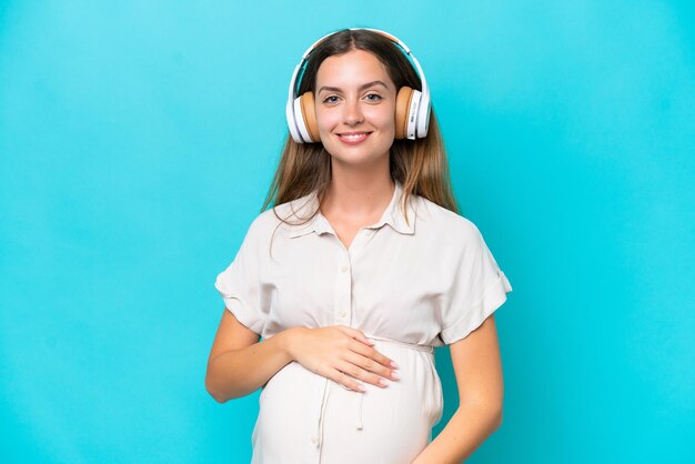 Young caucasian woman isolated on blue background pregnant and listening music