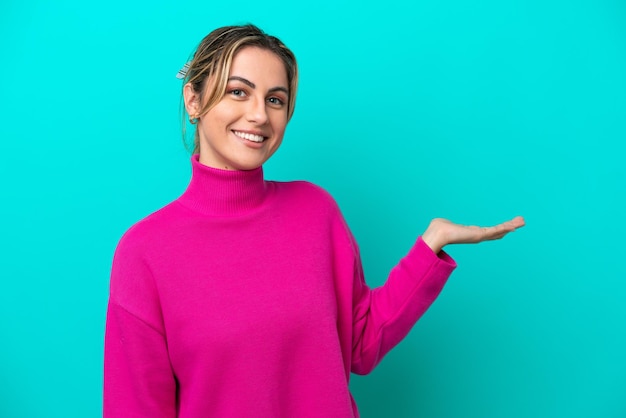 Young caucasian woman isolated on blue background presenting an idea while looking smiling towards