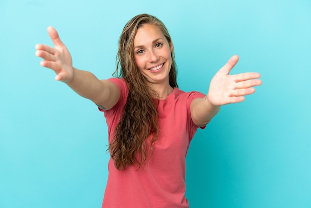 Young caucasian woman isolated on blue background presenting and inviting to come with hand