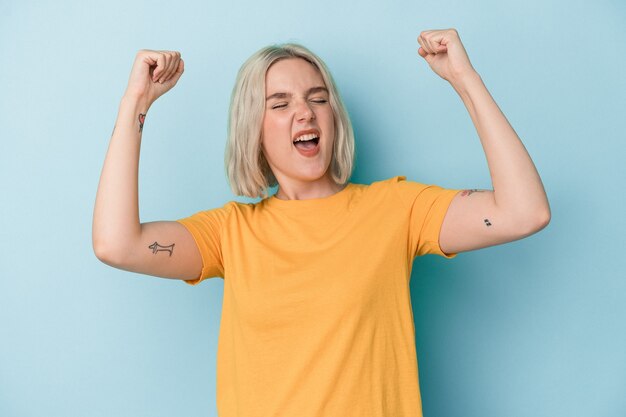 Young caucasian woman isolated on blue background raising fist after a victory, winner concept.