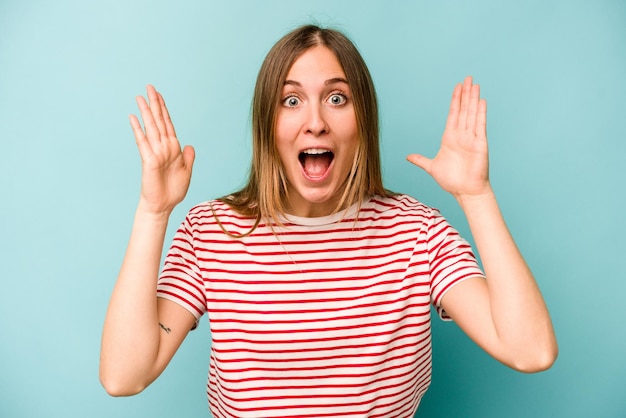 Young caucasian woman isolated on blue background receiving a pleasant surprise excited and raising hands