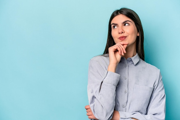 Young caucasian woman isolated on blue background relaxed thinking about something looking at a copy space