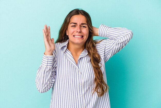 Young caucasian woman isolated on blue background  screaming with rage.