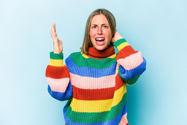 Young caucasian woman isolated on blue background screaming with rage