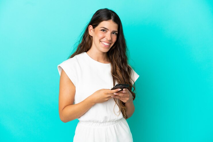 Photo young caucasian woman isolated on blue background sending a message with the mobile