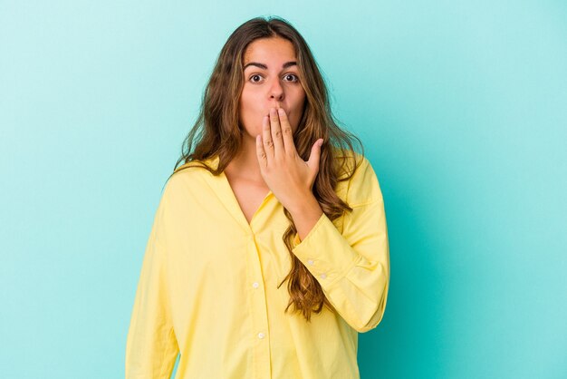 Young caucasian woman isolated on blue background  shocked, covering mouth with hands, anxious to discover something new.