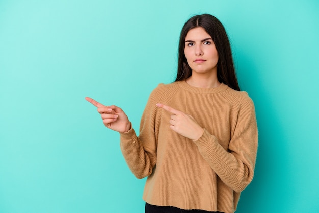 Young caucasian woman isolated on blue background shocked pointing with index fingers to a copy space.