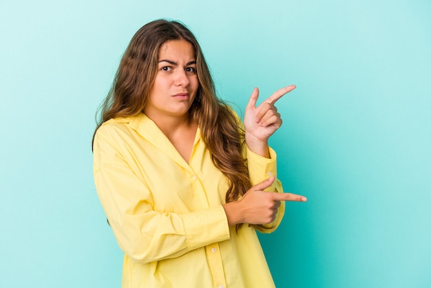 Young caucasian woman isolated on blue background  shocked pointing with index fingers to a copy space.