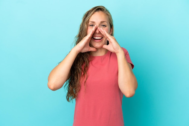 Young caucasian woman isolated on blue background shouting and announcing something