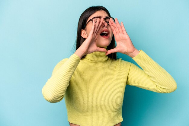 Young caucasian woman isolated on blue background shouting excited to front