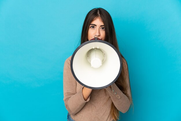 Foto giovane donna caucasica isolata su priorità bassa blu che grida tramite un megafono per annunciare qualcosa