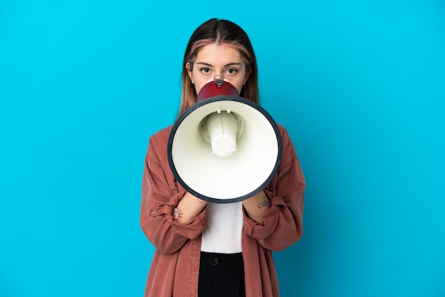 Young caucasian woman isolated on blue background shouting through a megaphone to announce something