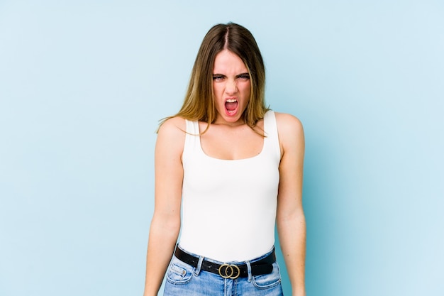 Young caucasian woman isolated on blue background shouting very angry, rage concept, frustrated.