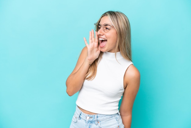 Young caucasian woman isolated on blue background shouting with\
mouth wide open to the side