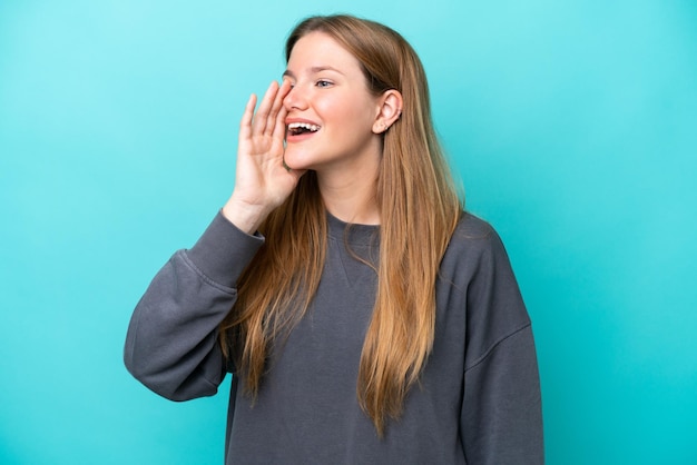 Young caucasian woman isolated on blue background shouting with mouth wide open to the side